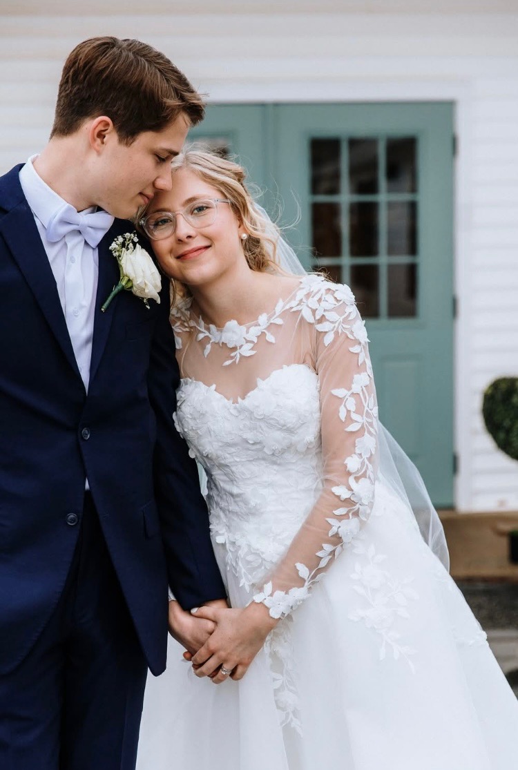 Sophie and William in wedding attire sharing a tender, close moment in front of a teal door at a white clapboard New England venue
